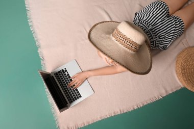 Plaj aksesuarları olan genç bir kadın yeşil arka planda dizüstü bilgisayar kullanıyor.