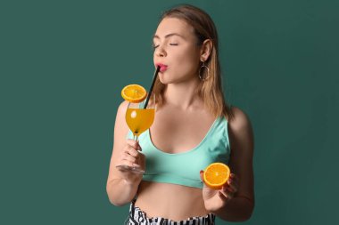 Yeşil arka planda portakal suyu kokteyli olan genç bir kadın.