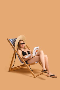 Güverte sandalyesinde bej arka planda gazete okuyan genç bir kadın