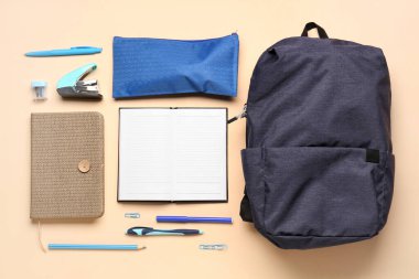 Sırt çantalı defterler, kalem kutusu ve soluk turuncu arka planda farklı kırtasiye malzemeleri.