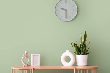 Odadaki yeşil duvarda ev bitkisi ve saati asılı modern raf ünitesi.