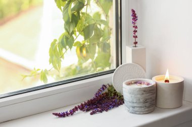 Yanan mumlar ve pencere eşiğinde adaçayı çiçekleri olan tutucular, yakın plan.