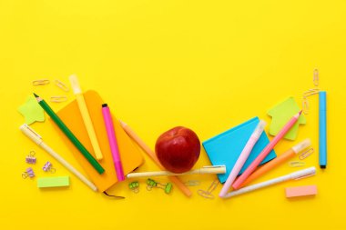 Sarı zemin üzerinde farklı kırtasiye malzemesi olan taze kırmızı elma.