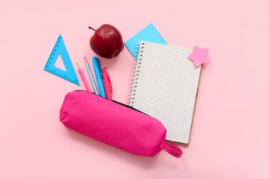 Taze kırmızı elma, kalem kutusu ve pembe arka planda farklı kırtasiye malzemesi olan defteri aç