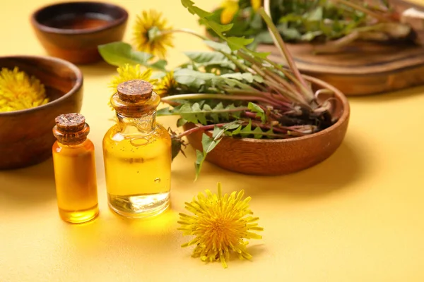 Stock image Bottles with cosmetic oil and bowls of dandelion flowers on yellow background