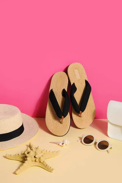 粉色墙壁附近有带太阳镜 旅行袋和柳条帽的折叠式拖鞋 — 图库照片