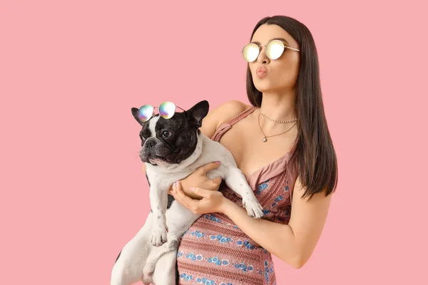 Young woman with her French bulldog in sunglasses on pink background