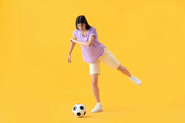 年轻女子在黄色背景下玩足球 — 图库照片