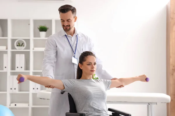 在康复中心与坐在轮椅上的年轻妇女一起工作的男性理疗师 — 图库照片