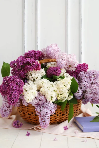 stock image Wicker basket with beautiful fragrant lilac flowers near white wooden wall