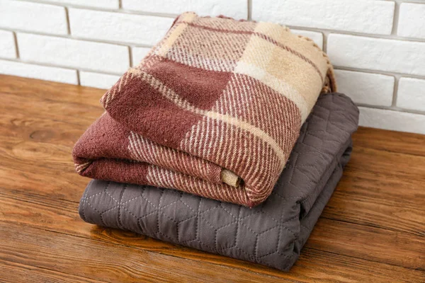 ライトレンガの壁の近くの木製テーブルの上に新しい柔らかい折り畳まれた毛布 — ストック写真