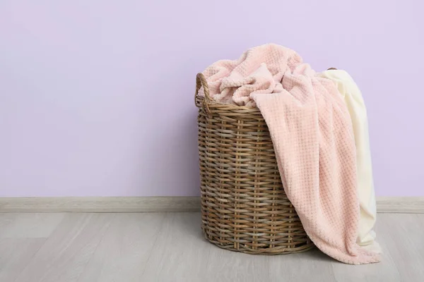 stock image Basket with new soft blanket near purple wall in room