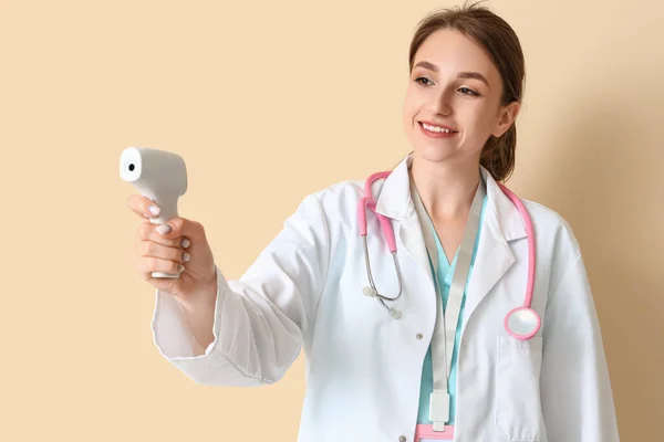 ベージュの背景に赤外線温度計を持つ女性医療インターン — ストック写真