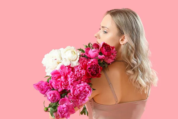 Pembe arka planda güzel şakayık çiçekleri olan genç bir kadın.