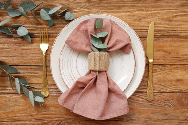 ユーカリの枝と木製のテーブルの上に折り畳まれたナプキンと美しいテーブルの設定 — ストック写真
