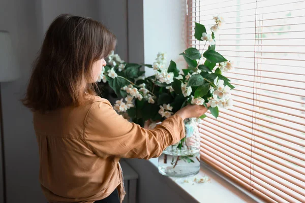 女人在窗台上的花瓶里欣赏着盛开的茉莉花 — 图库照片