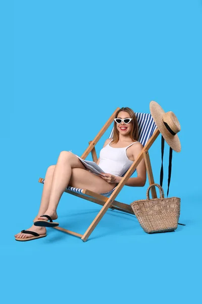 年轻女子 穿着蓝色背景的躺椅 头戴报纸和海滩饰物 — 图库照片