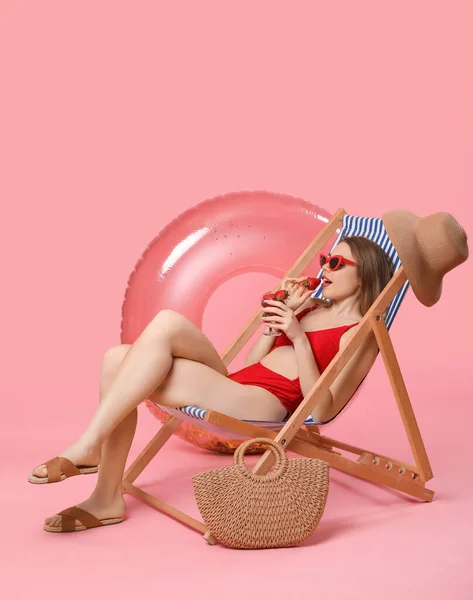 年轻女子与海滩配件吃草莓在甲板上的椅子粉红色背景 — 图库照片