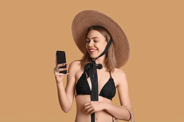 stock image Young woman in swimsuit using mobile phone on beige background