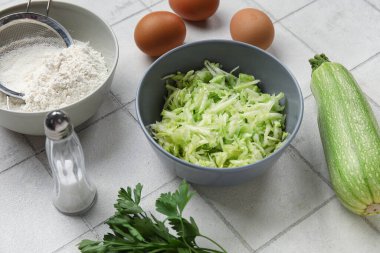 Beyaz fayanslı börek hazırlamak için rendelenmiş kabak, un ve yumurta kâseleri.