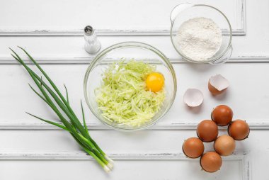 Beyaz ahşap arka planda börek hazırlamak için rendelenmiş kabak ve malzemelerle dolu bir kase.