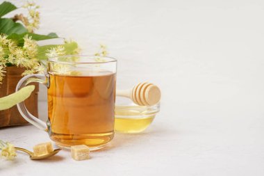 Beyaz zemin üzerinde bal olan bir bardak ıhlamur çayı ve kase.