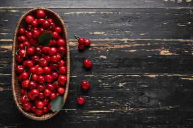 Siyah ahşap arka planda kirazlı hasır kase.