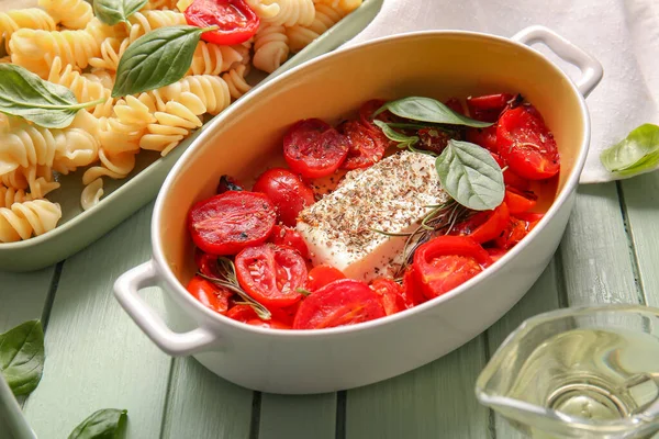 Stock image Baking dish with tasty tomatoes, feta cheese and pasta on green wooden background