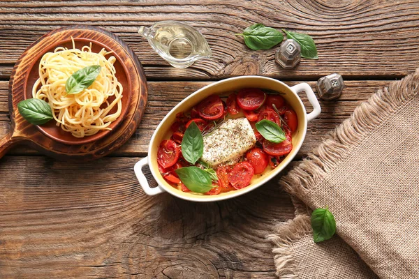 stock image Baking dish with tasty tomatoes, feta cheese and pasta on wooden background