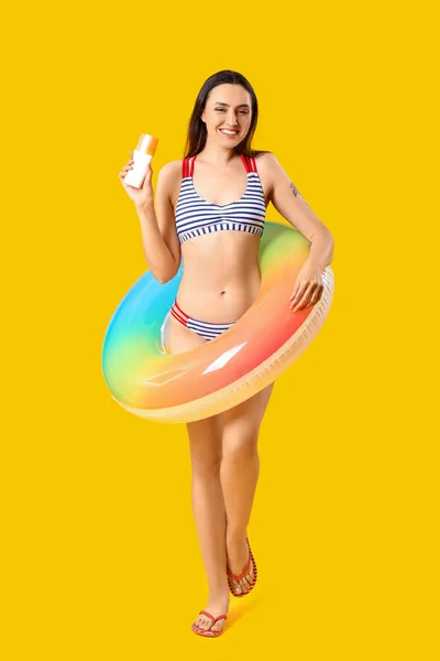 日焼け止めクリームと黄色の背景にインフレータブルリングを持つ若い女性 — ストック写真