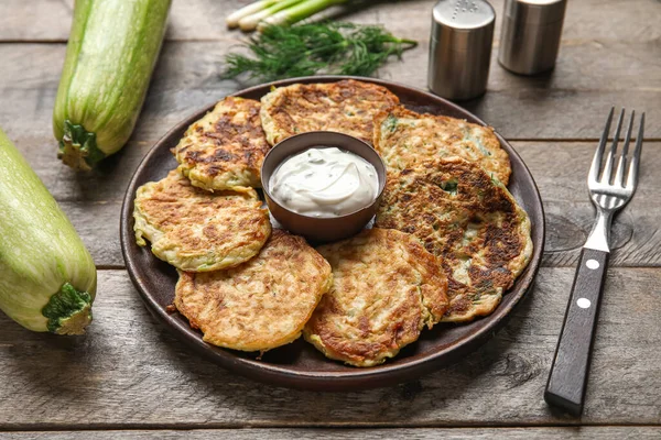 stock image Plate of tasty zucchini fritters with sour cream on wooden background