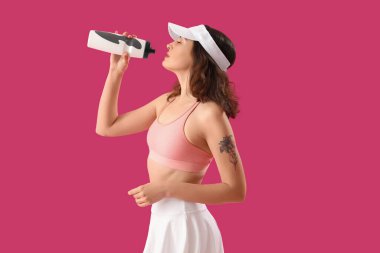 Pembe arka planda bir şişe suyu olan genç bir kadın.