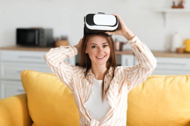 VR gözlüklü güzel bir kadın evdeki kanepede oturuyor.