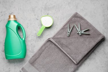 Çamaşır deterjanları, çamaşır mandalları ve gri grunge arka planda havlu.