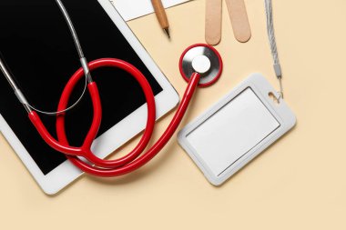 Sarı arkaplanda stetoskop, tablet bilgisayar ve rozet