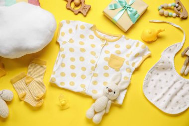 Bebek kıyafetleri ve sarı arka planda oyuncakları olan kompozisyon