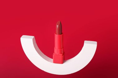 Kırmızı arka planda dekoratif alçı podyum ve ruj.