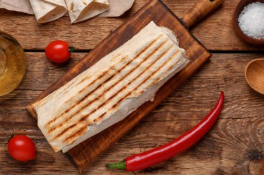 Ahşap arka planda domatesli lezzetli shawarma panosu.