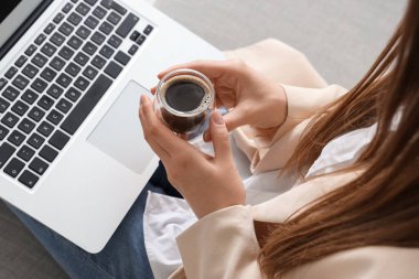 Kanepede oturan modern dizüstü bilgisayarı ve bir bardak lezzetli kahvesi olan bir kadın.