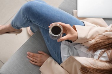 Bir bardak lezzetli kahveyle kanepede oturan kadın.