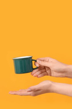 Sarı arka planda kadın eli bardağı tutuyor.