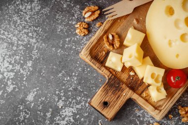 Gri arkaplanda İsviçre peyniri ve domates parçaları olan tahta