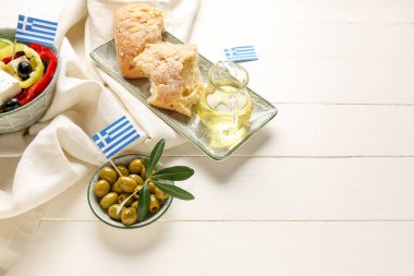 Beyaz ahşap masada ciabatta ekmeği, salata, yeşil zeytin ve Yunanistan bayrakları bulunan tabaklar