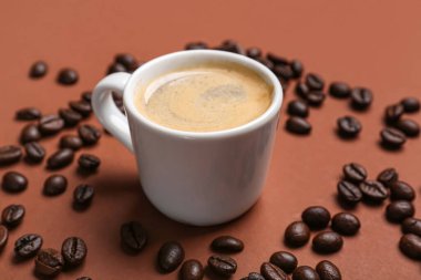 Kahverengi arka planda bir fincan sıcak espresso ve kahve çekirdeği.