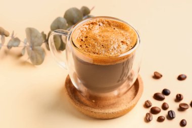 Bir bardak sıcak espresso ve bej arka planda okaliptüslü kahve çekirdekleri.