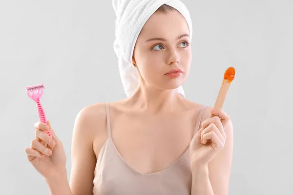 stock image Young woman choosing between shaving and sugaring on light background