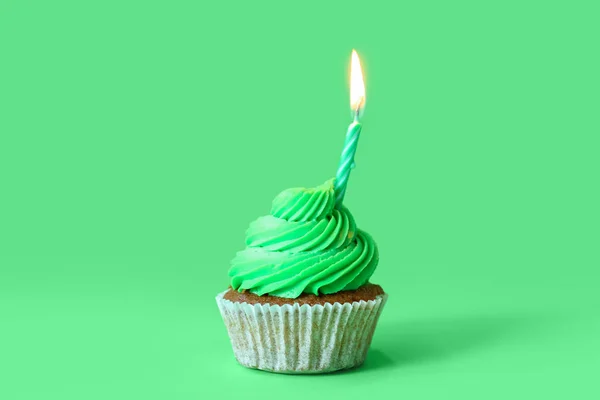 Tasty cupcake with birthday candle on green background