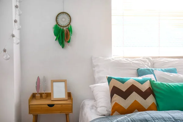 ベッド ベッドサイドテーブルと夢のキャッチャーが白い壁にぶら下がっているモダンなベッドルームのインテリア — ストック写真