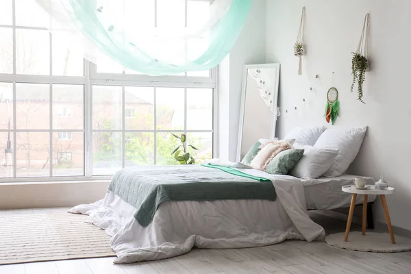 stock image Interior of modern bedroom with bed, mirror and dream catcher hanging on light wall