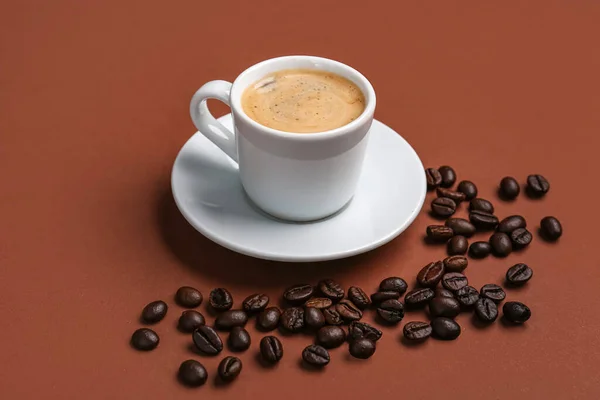 茶色の背景に熱いエスプレッソとコーヒー豆のカップ — ストック写真